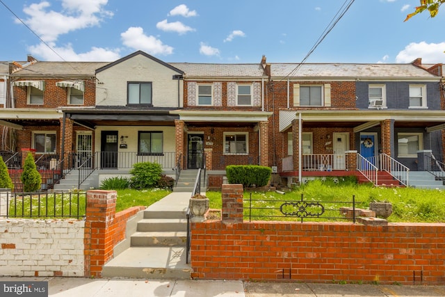 townhome / multi-family property featuring covered porch, brick siding, and a fenced front yard
