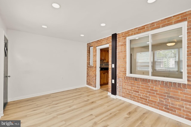 unfurnished room with recessed lighting, baseboards, light wood finished floors, and brick wall