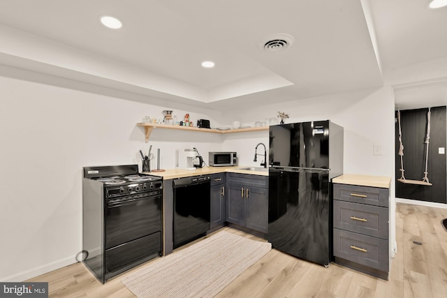 kitchen with a sink, baseboards, light wood-type flooring, visible vents, and black appliances