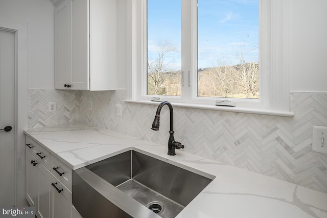 kitchen featuring a sink, white cabinetry, decorative backsplash, and light stone countertops