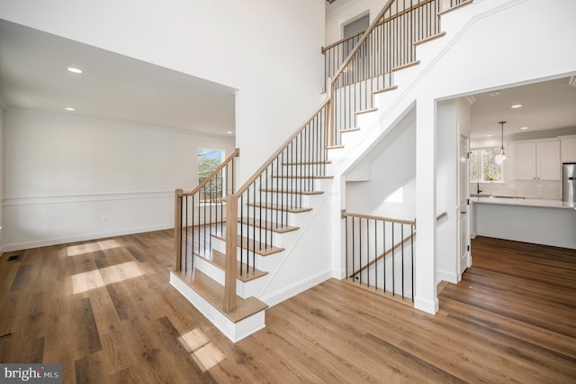 stairs featuring baseboards, recessed lighting, wood finished floors, and a towering ceiling