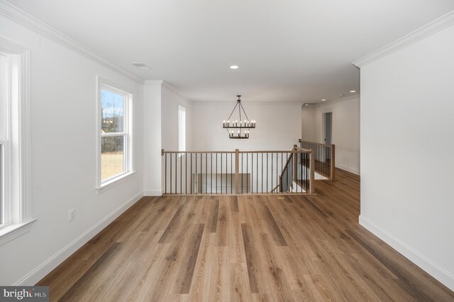 spare room featuring an inviting chandelier, ornamental molding, baseboards, and wood finished floors