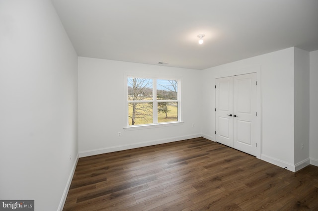 unfurnished bedroom with dark wood-style flooring, baseboards, and a closet
