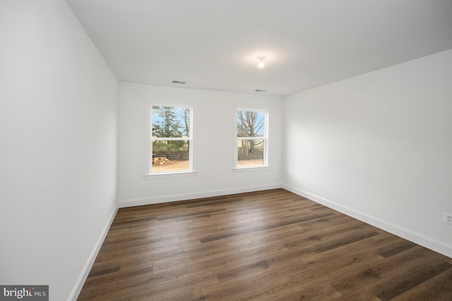 empty room with baseboards, visible vents, and dark wood-style floors