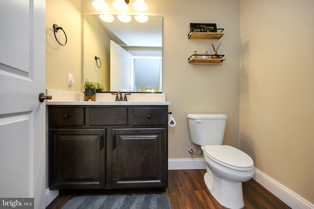 half bathroom with vanity, baseboards, wood finished floors, and toilet