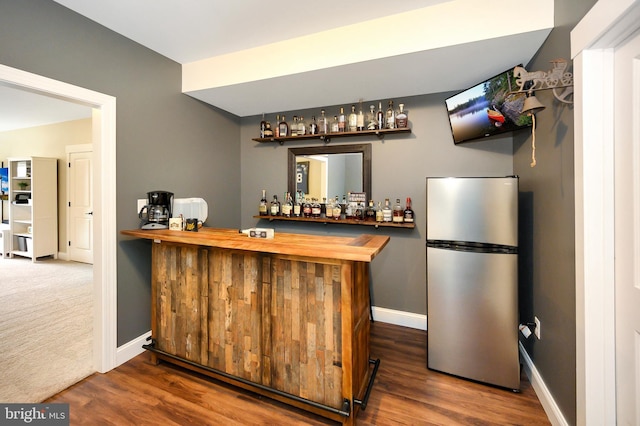bar with baseboards, freestanding refrigerator, a bar, and wood finished floors