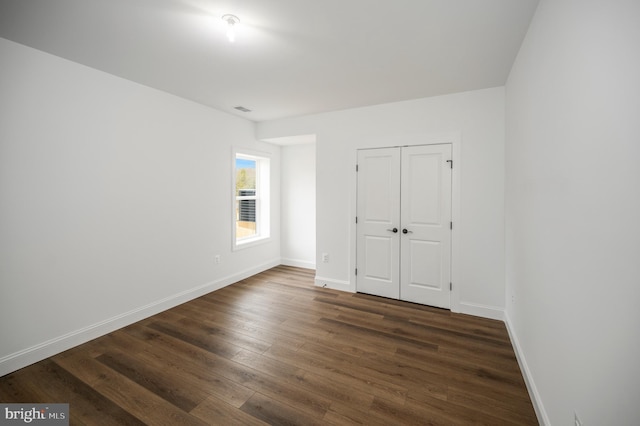 unfurnished bedroom featuring baseboards, dark wood finished floors, visible vents, and a closet