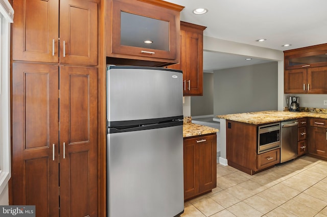 kitchen with light tile patterned floors, glass insert cabinets, light stone countertops, and stainless steel appliances