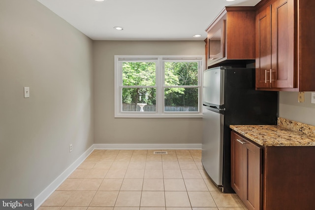 kitchen featuring visible vents, freestanding refrigerator, baseboards, and light stone counters