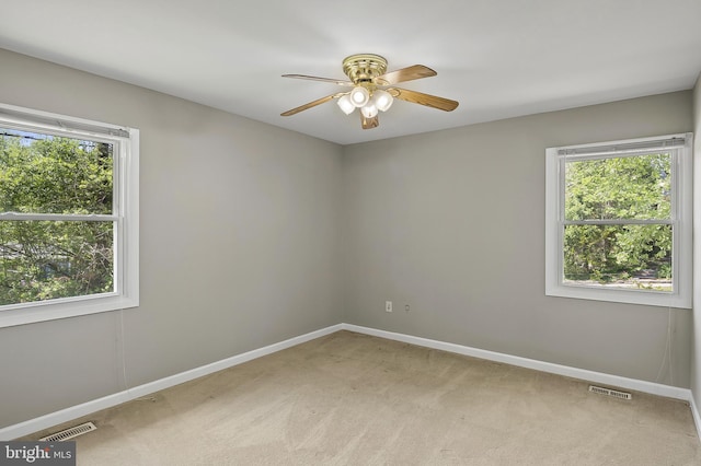 spare room featuring visible vents, a ceiling fan, baseboards, and light carpet