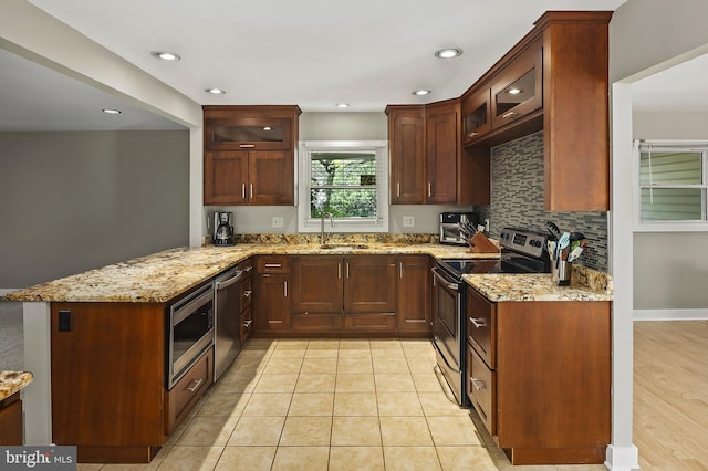 kitchen with light stone countertops, a sink, stainless steel appliances, a peninsula, and glass insert cabinets
