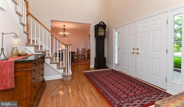 entrance foyer featuring a chandelier, wood-type flooring, stairs, a towering ceiling, and baseboards