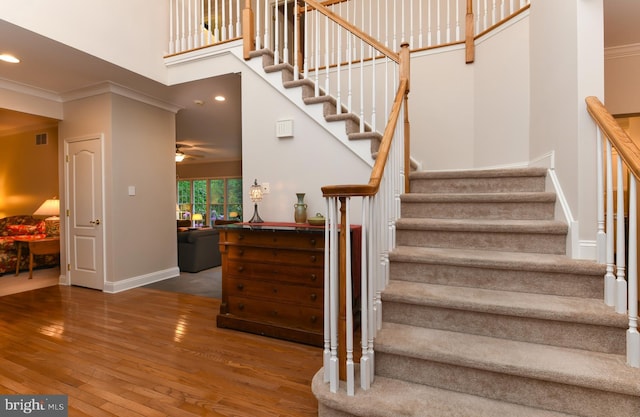 stairway featuring hardwood / wood-style flooring, a ceiling fan, baseboards, a high ceiling, and crown molding