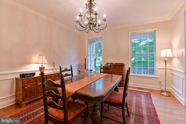 dining area featuring light wood-style flooring, a chandelier, ornamental molding, plenty of natural light, and a decorative wall