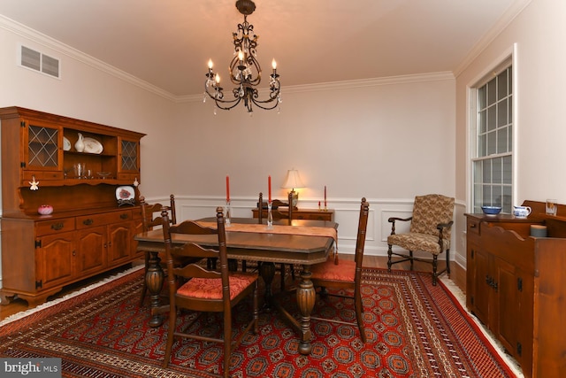 dining space with crown molding, a chandelier, wood finished floors, and wainscoting