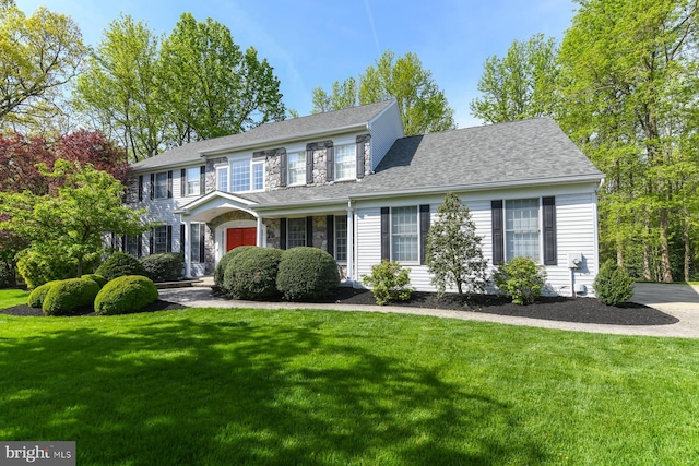 colonial home featuring a front yard, roof with shingles, and stone siding