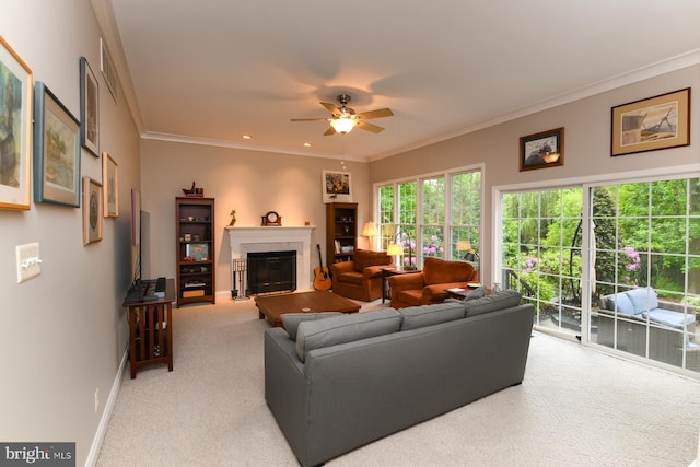 living area with carpet flooring, a glass covered fireplace, baseboards, a ceiling fan, and ornamental molding