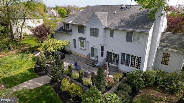 rear view of house with entry steps, roof with shingles, a patio, and a chimney