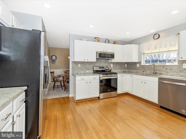 kitchen featuring light wood-type flooring, white cabinets, a sink, appliances with stainless steel finishes, and backsplash