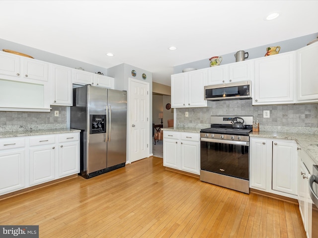 kitchen with appliances with stainless steel finishes, tasteful backsplash, light stone counters, light wood finished floors, and white cabinetry
