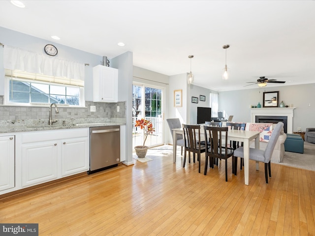 kitchen with stainless steel dishwasher, light wood-style floors, white cabinets, tasteful backsplash, and a sink