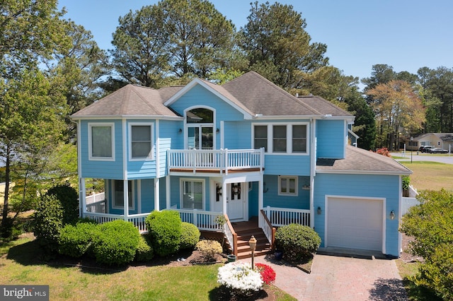 colonial-style house with an attached garage, a balcony, decorative driveway, roof with shingles, and a porch