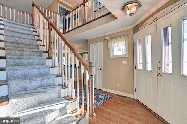 foyer entrance featuring crown molding, baseboards, visible vents, and stairway
