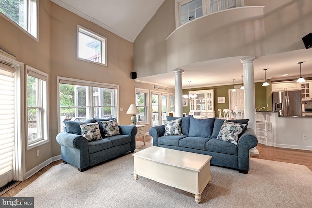 living room with decorative columns, wood finished floors, baseboards, high vaulted ceiling, and a chandelier