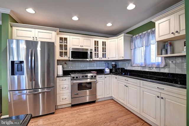 kitchen with crown molding, light wood finished floors, appliances with stainless steel finishes, and glass insert cabinets
