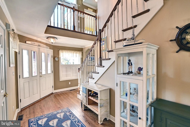 foyer entrance with crown molding, wood finished floors, baseboards, a high ceiling, and french doors