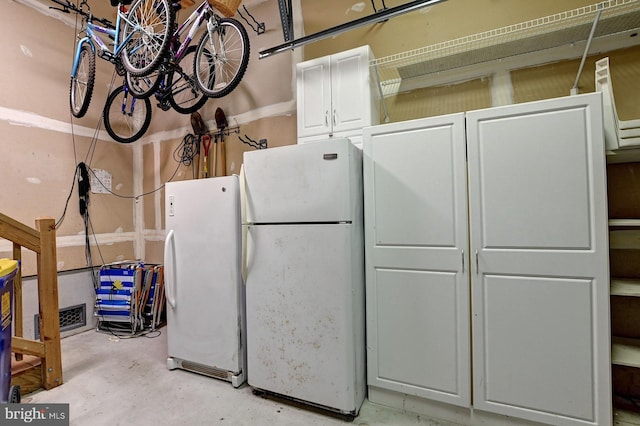 interior space with freestanding refrigerator, white cabinets, and concrete floors