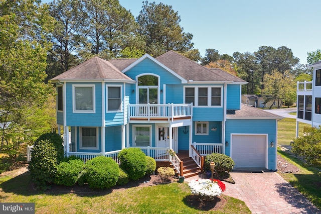 view of front of house with a balcony, covered porch, decorative driveway, roof with shingles, and an attached garage