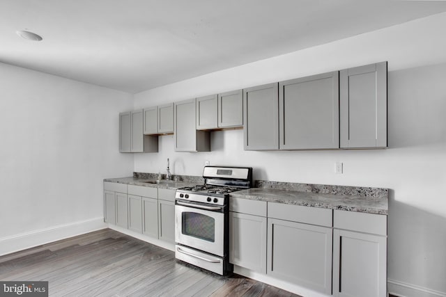 kitchen with a sink, baseboards, gas range, gray cabinetry, and dark wood-style floors