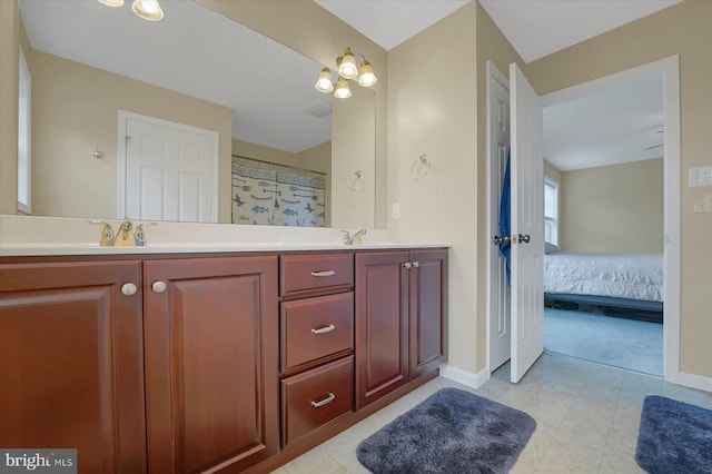 ensuite bathroom with double vanity, connected bathroom, baseboards, and a sink