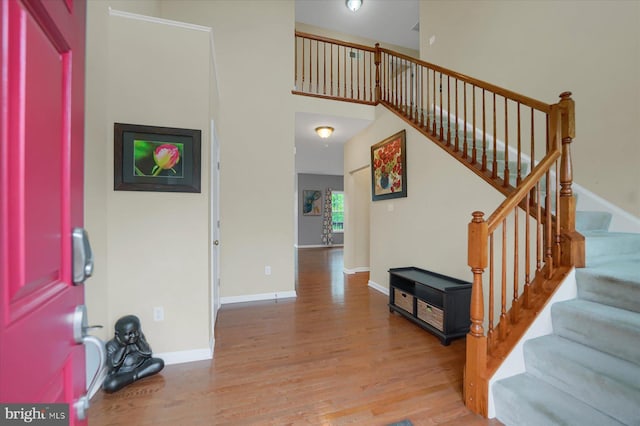 foyer entrance featuring stairway, light wood-style flooring, baseboards, and a towering ceiling