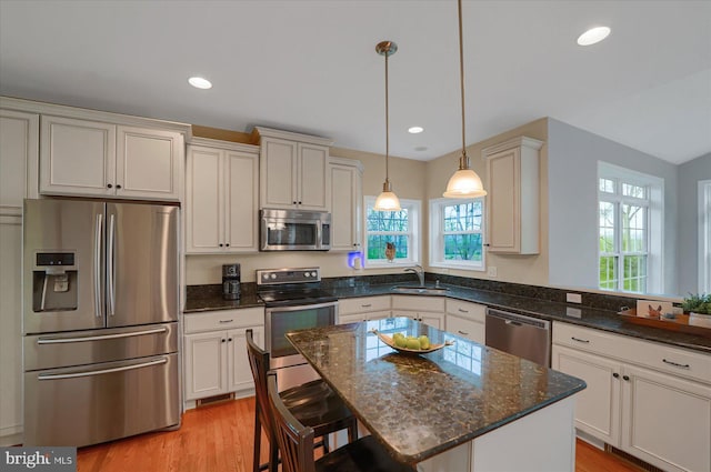 kitchen featuring a sink, dark stone counters, light wood-style flooring, a kitchen bar, and appliances with stainless steel finishes