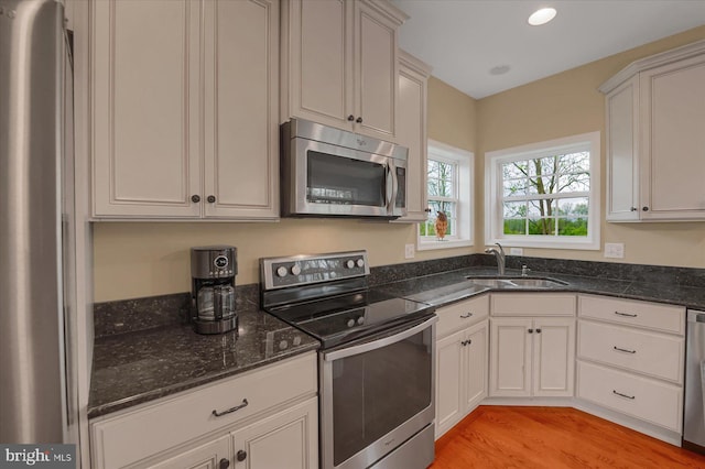 kitchen featuring a sink, stainless steel appliances, dark stone countertops, recessed lighting, and light wood finished floors