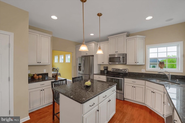 kitchen featuring a sink, appliances with stainless steel finishes, white cabinets, a kitchen island, and light wood-style floors