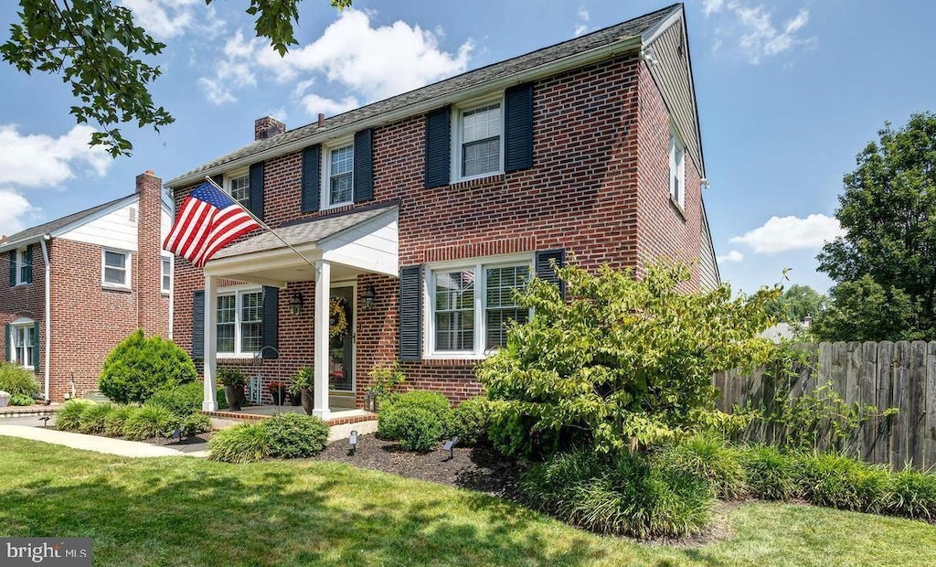 view of front of home with brick siding, a front lawn, fence, and a chimney