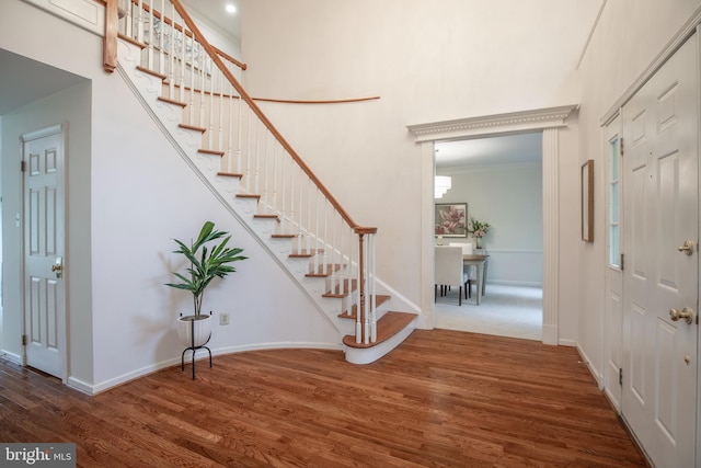 entryway with wood finished floors, stairs, baseboards, a towering ceiling, and crown molding