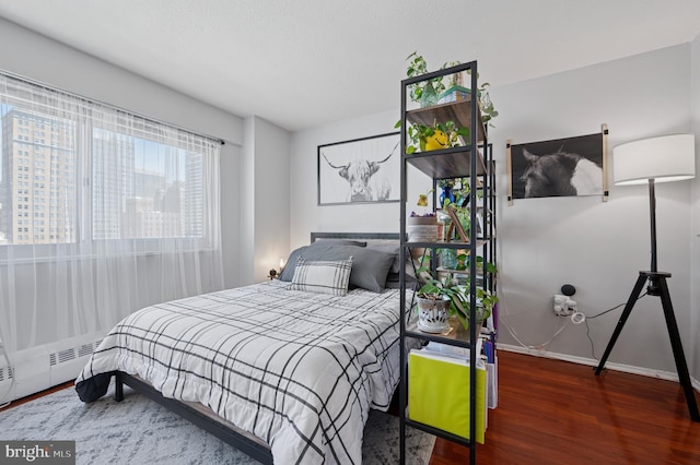 bedroom with baseboards, a baseboard heating unit, and wood finished floors