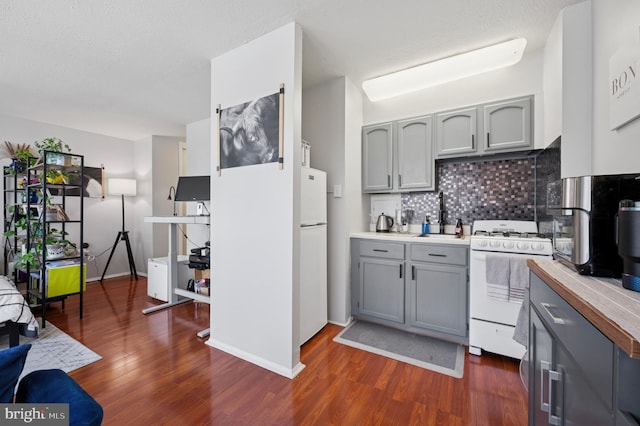 kitchen with dark wood-type flooring, decorative backsplash, gray cabinets, and white appliances