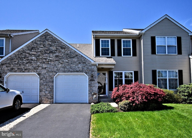 traditional-style home featuring a garage, a front yard, driveway, and stone siding