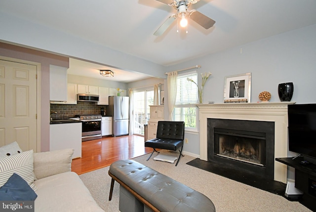 living area with a fireplace with flush hearth and ceiling fan