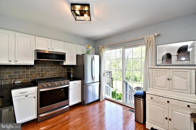 kitchen with appliances with stainless steel finishes, white cabinets, wood-type flooring, and backsplash