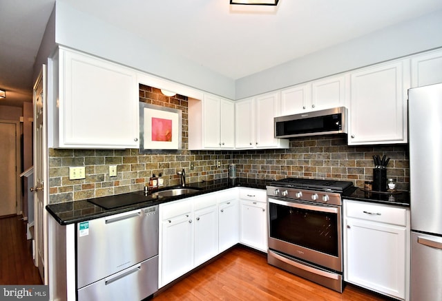 kitchen with backsplash, dark countertops, a sink, white cabinets, and stainless steel appliances