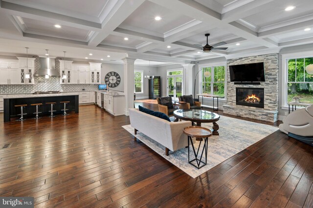 living room featuring coffered ceiling, a ceiling fan, a stone fireplace, and dark wood-type flooring