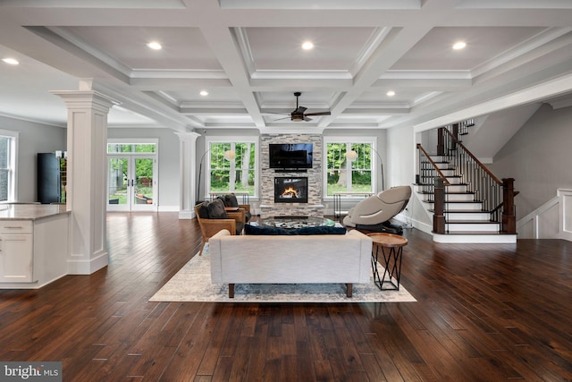 living room featuring dark wood finished floors, a stone fireplace, stairs, a ceiling fan, and ornate columns