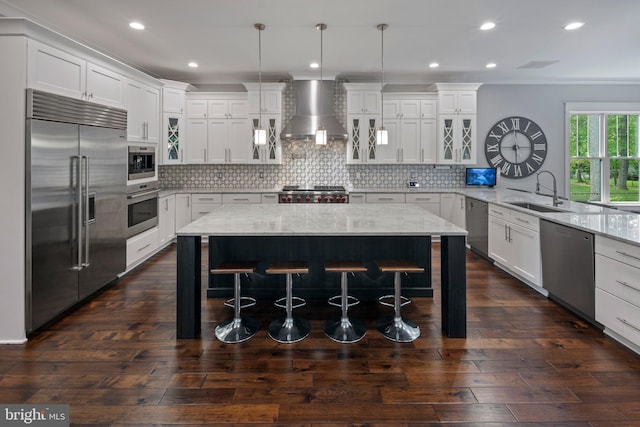 kitchen with white cabinets, appliances with stainless steel finishes, a sink, a breakfast bar area, and wall chimney exhaust hood