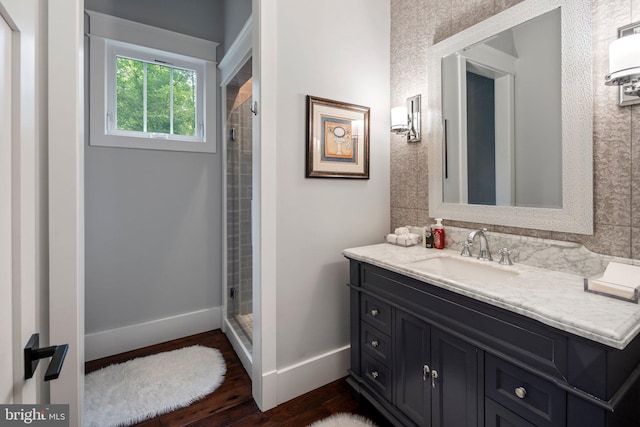 bathroom featuring vanity, baseboards, wood finished floors, and a stall shower